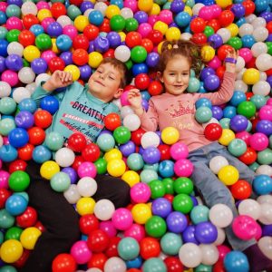 Brother with sister playing in colorful ball pit.